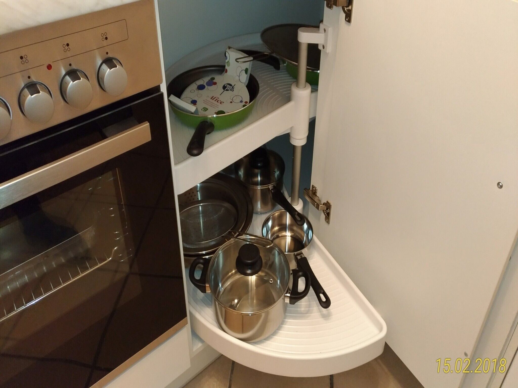 A compact kitchen with a built-in oven, a shelf with cookware, and a white countertop.