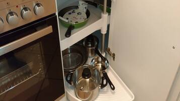 A compact kitchen with a built-in oven, a shelf with cookware, and a white countertop.