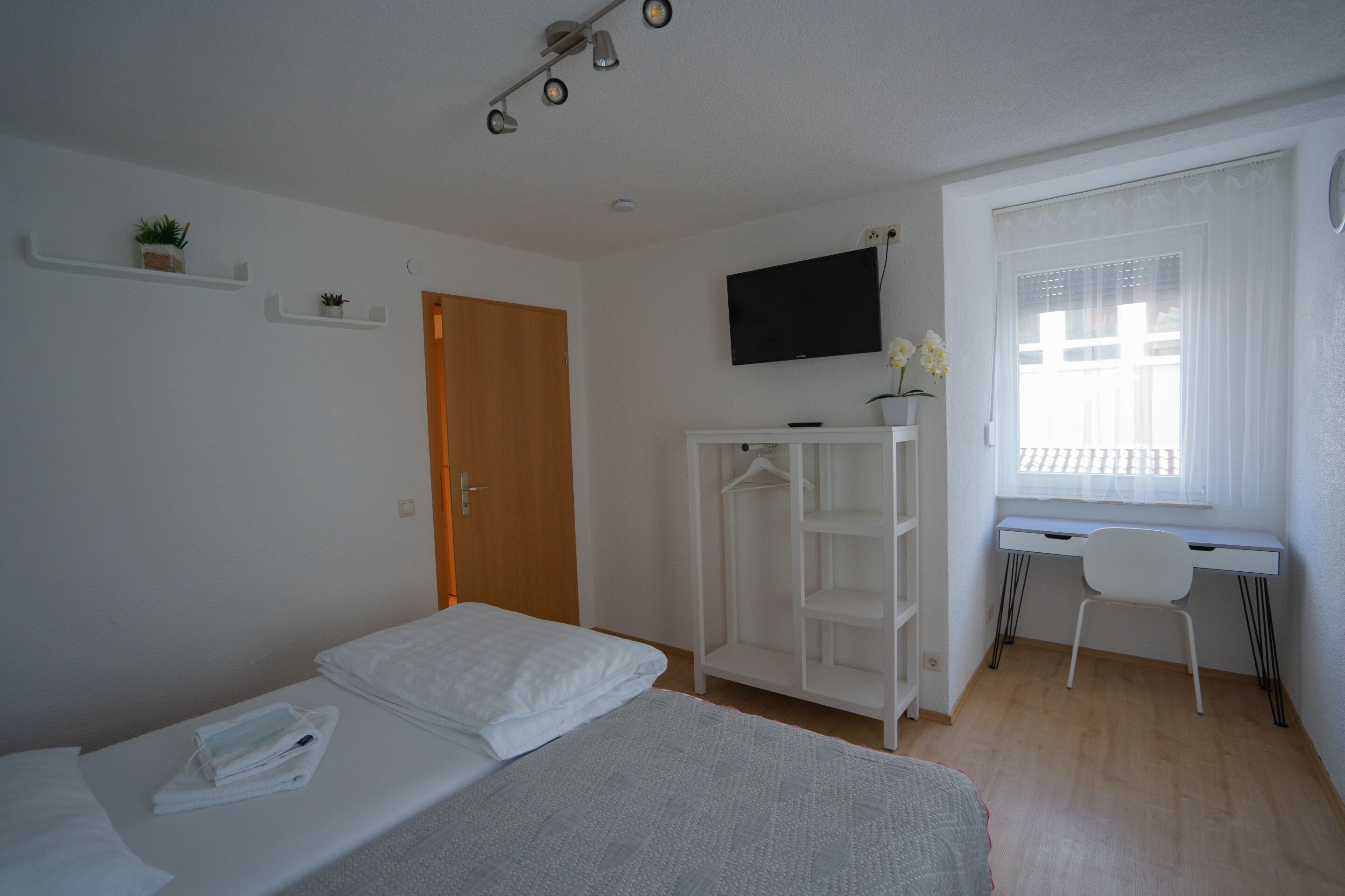 A bedroom with a bed, a desk, a TV, and a window.