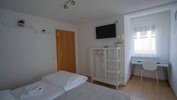 A bedroom with a bed, a desk, a TV, and a window.