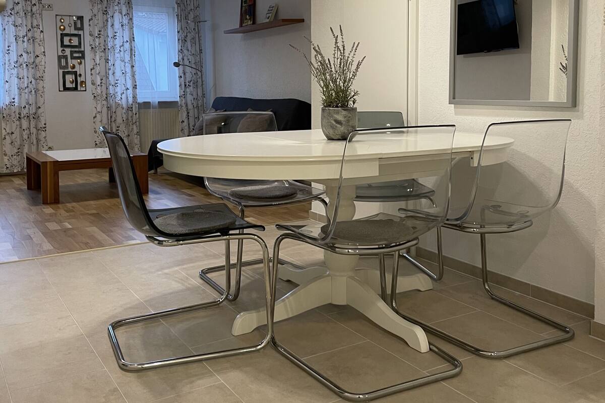 Et moderne spiseområde med et rundt bord, gennemsigtige stole og et stort spejl.