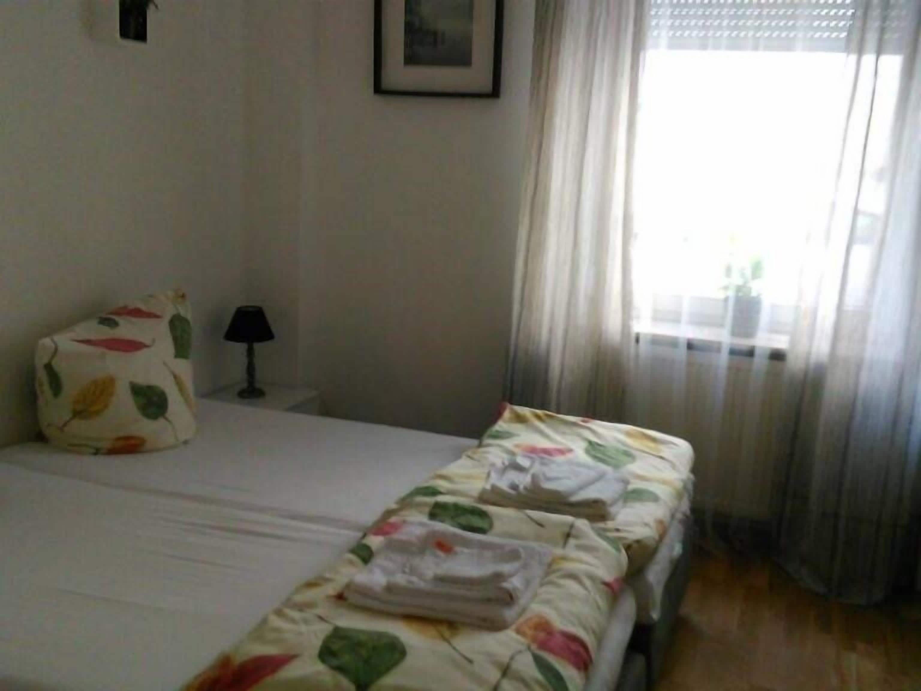 Una habitación de hotel con cama, mesita de noche, lámpara y ventana con cortinas.