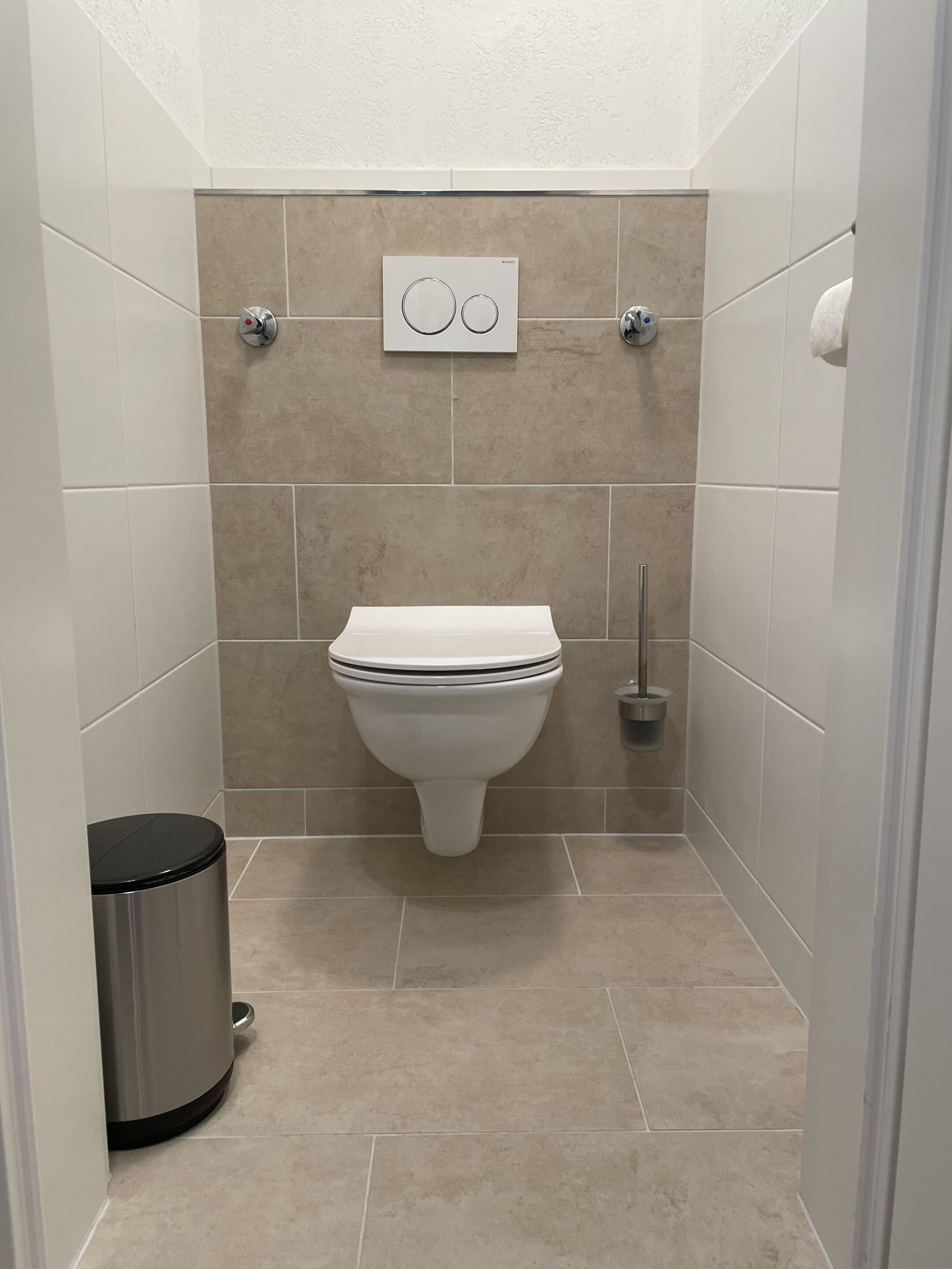 Une petite salle de bain moderne, équipée de toilettes, d’une poubelle et d’un sèche-mains fixé au mur.