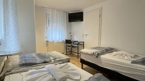 A hotel room with two beds, a desk, a chair, a TV mounted on the wall, and a window with curtains. - Fewo Reutlingen Metzstrasse (Reutlingen)