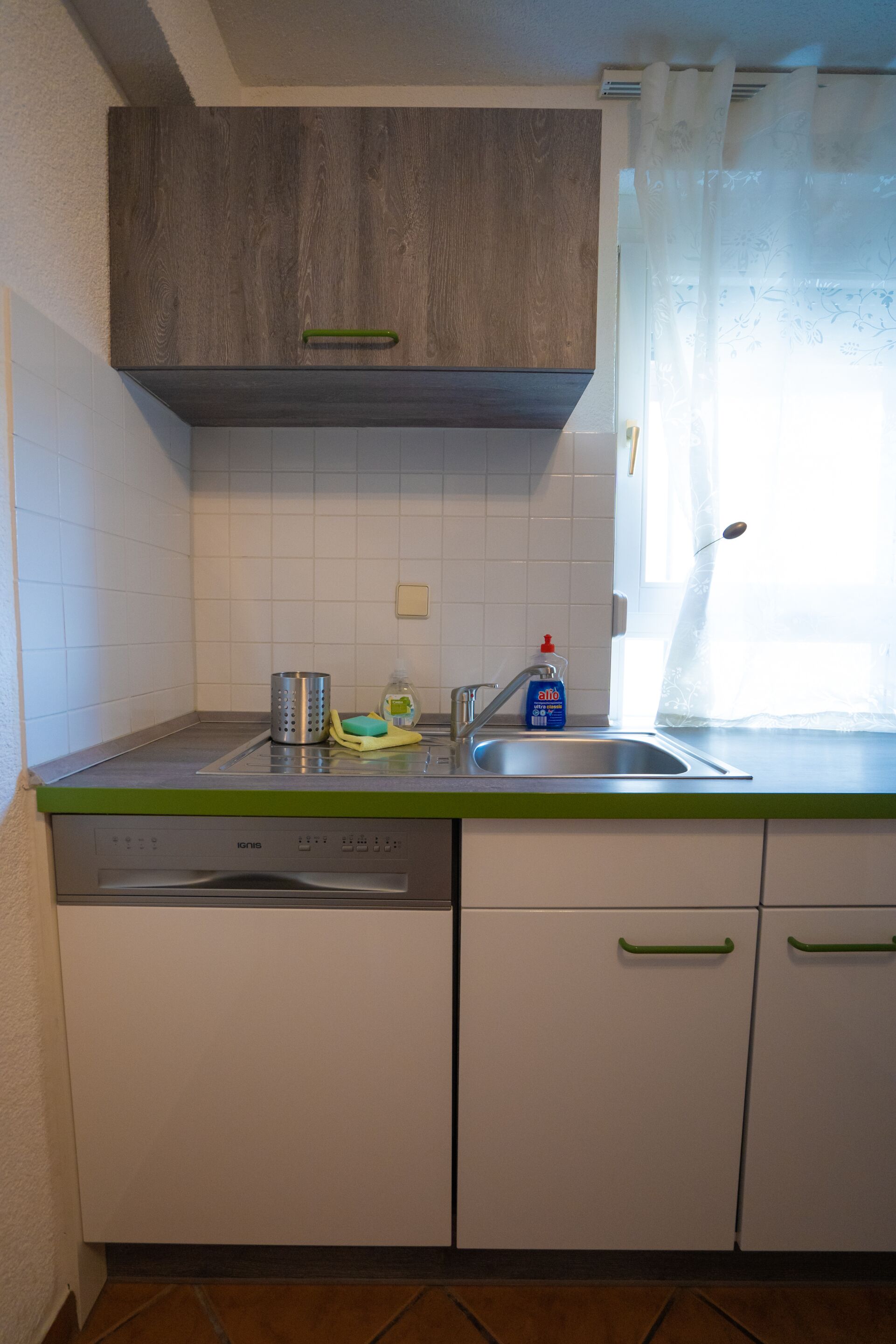Eine Küche mit weißen Schränken, einem Geschirrspüler, einer Spüle und einem Fenster mit Vorhang.
