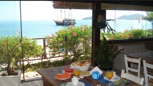 Una mesa servida con alimentos para el desayuno, vista al mar y un barco a lo lejos.
