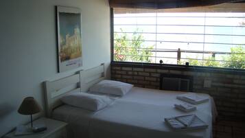 Quarto com cama grande, mesa de cabeceira com abajur e um quadro na parede.