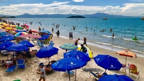 Una playa con muchos sombrillas y sillas, gente nadando y tomando el sol.