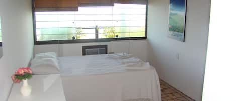 A bedroom with a bed, a small table with a vase of flowers, a radiator, and a window with blinds.