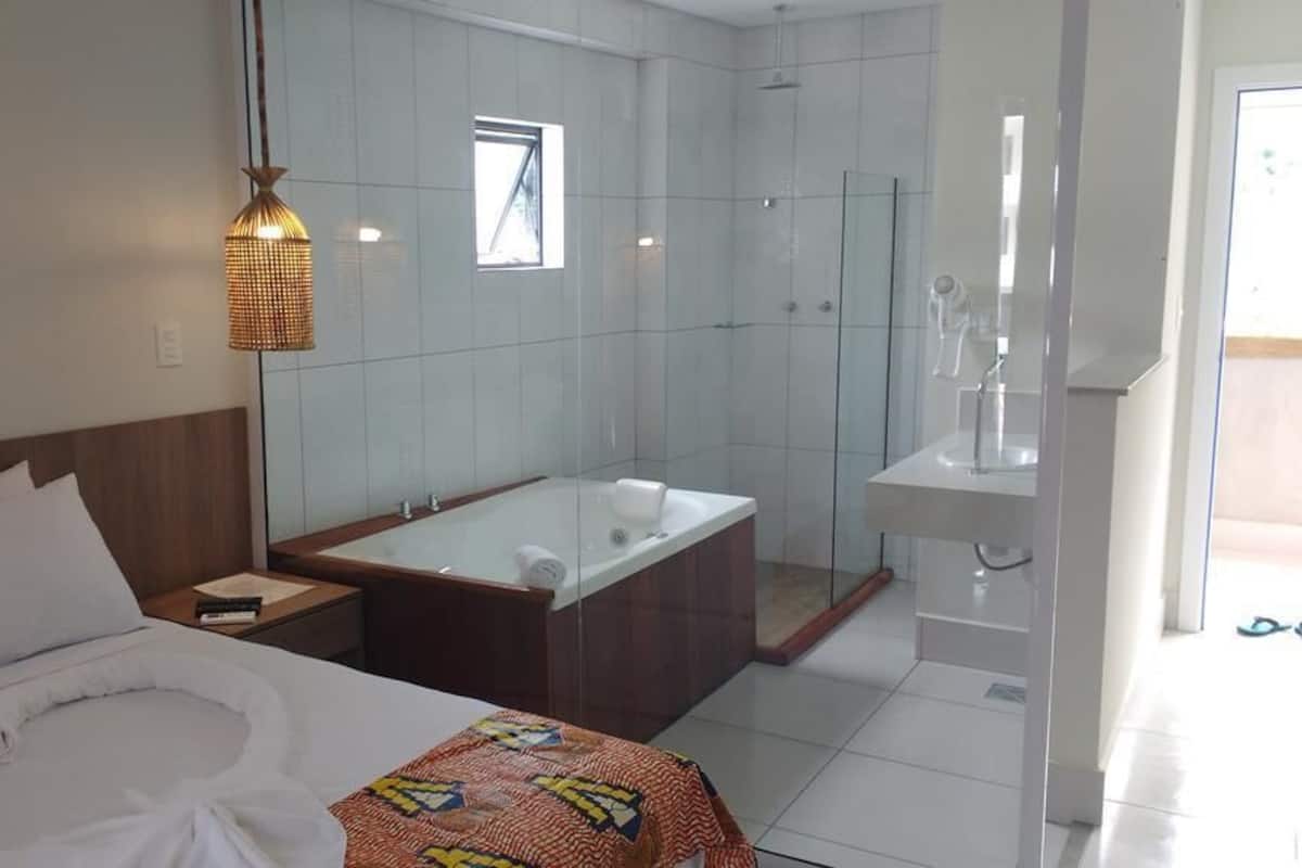 Ein modernes Hotelzimmer mit einem großen Bett, einer Badewanne, einer Dusche und einem Badezimmer inklusive Waschbecken und Spiegel.