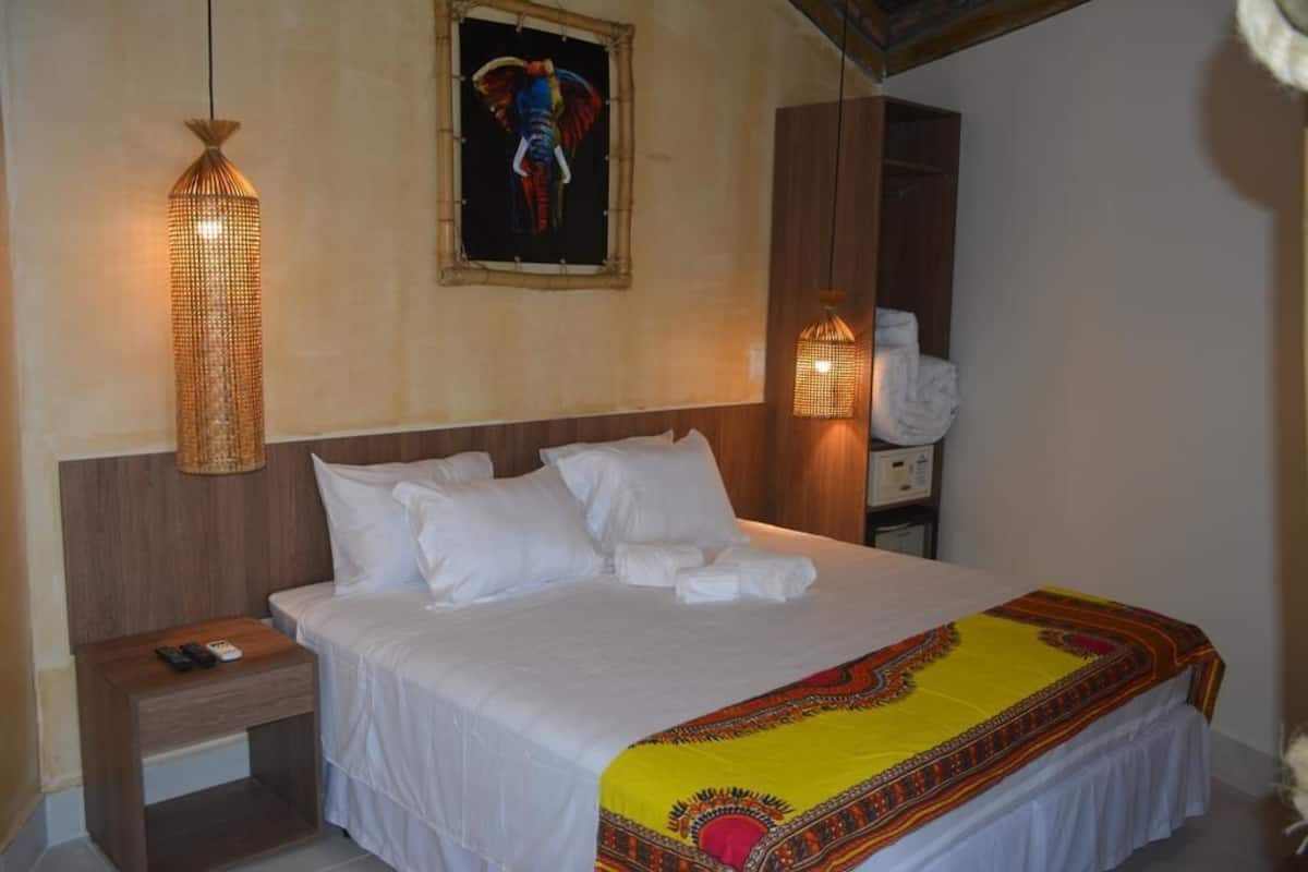 Ein Hotelzimmer mit einem Bett, einem Nachttisch, einer Lampe und einem Elefantenbild an der Wand.
