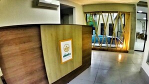Un área de recepción con un mostrador de madera, el logotipo en un marco y vistas a una piscina a través de un panel de vidrio.