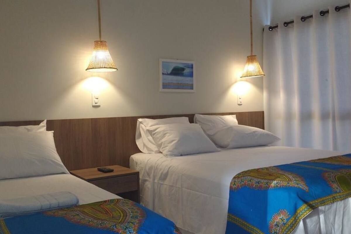 Ein Hotelzimmer mit zwei Betten, jeweils mit weißer Bettwäsche und einer blau gemusterten Tagesdecke. Zwei Nachttischlampen, ein Nachttisch und ein gerahmtes Bild hängen an der Wand.