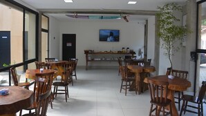 Un restaurante con mesas y sillas de madera, un televisor en la pared y una planta a la derecha.