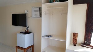 Une pièce avec un téléviseur fixé au mur, un petit réfrigérateur blanc, une étagère avec un magazine et un vase décoratif.