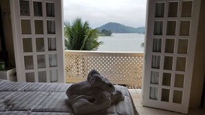 Un balcon avec vue sur un lac et des montagnes, un lit avec une serviette enroulée, et une cloison en treillis de bois.