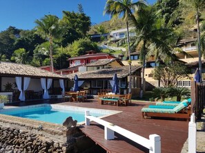 A pool area with wooden deck, lounge chairs, and umbrellas. - Pousada Costa do Sape (Angra dos Reis)