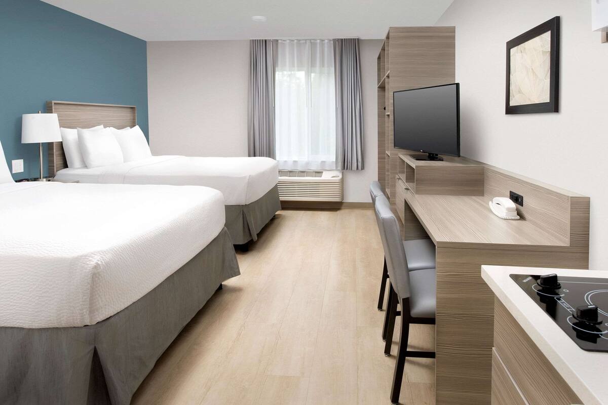 Une chambre d’hôtel avec deux lits, une télévision, un bureau avec une chaise et une fenêtre avec des rideaux.