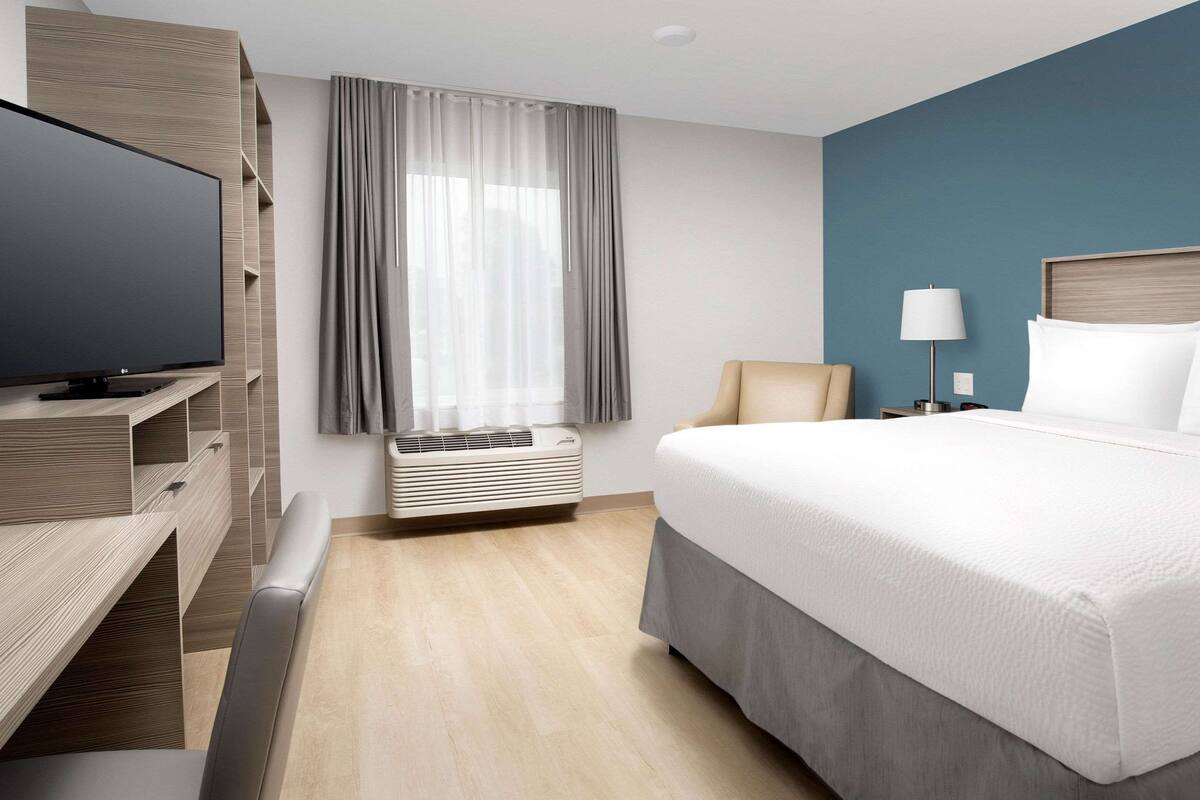 Une chambre d’hôtel moderne dotée d’un grand lit, d’un téléviseur à écran plat, d’un bureau avec une chaise, d’une lampe et d’une fenêtre avec des rideaux.