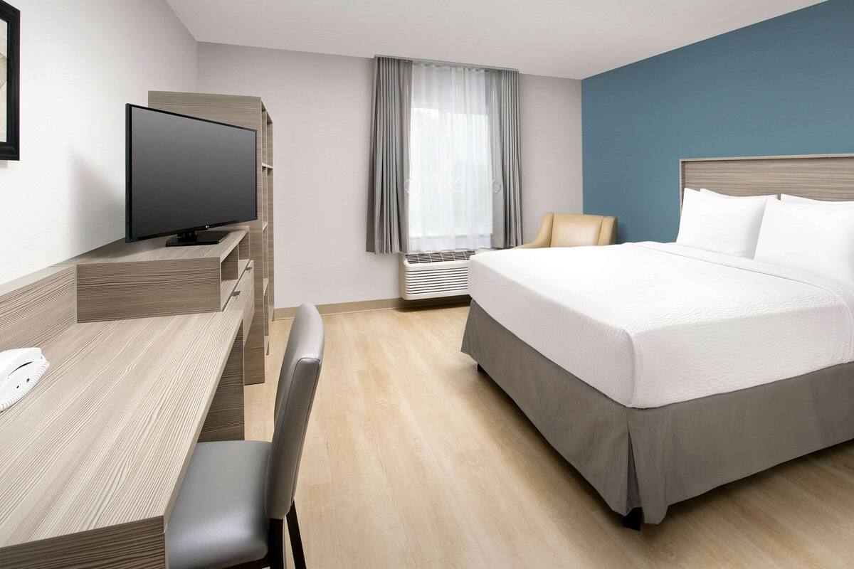 Une chambre d’hôtel comprenant un lit, un bureau avec une chaise, une télévision et une fenêtre avec des rideaux.
