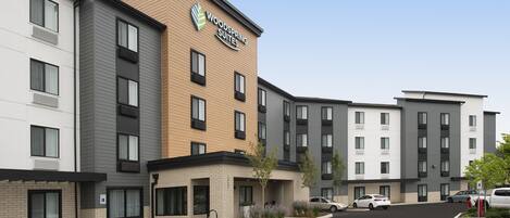 A multi-story hotel with a prominent "Woodspring Suites" sign, a parking lot, and several cars parked in front.