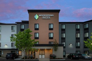 A hotel named Woodspring Suites with a modern design, featuring a prominent logo, multiple windows, and a parking lot with cars. - WoodSpring Suites Seattle Tukwila (Tukwila)