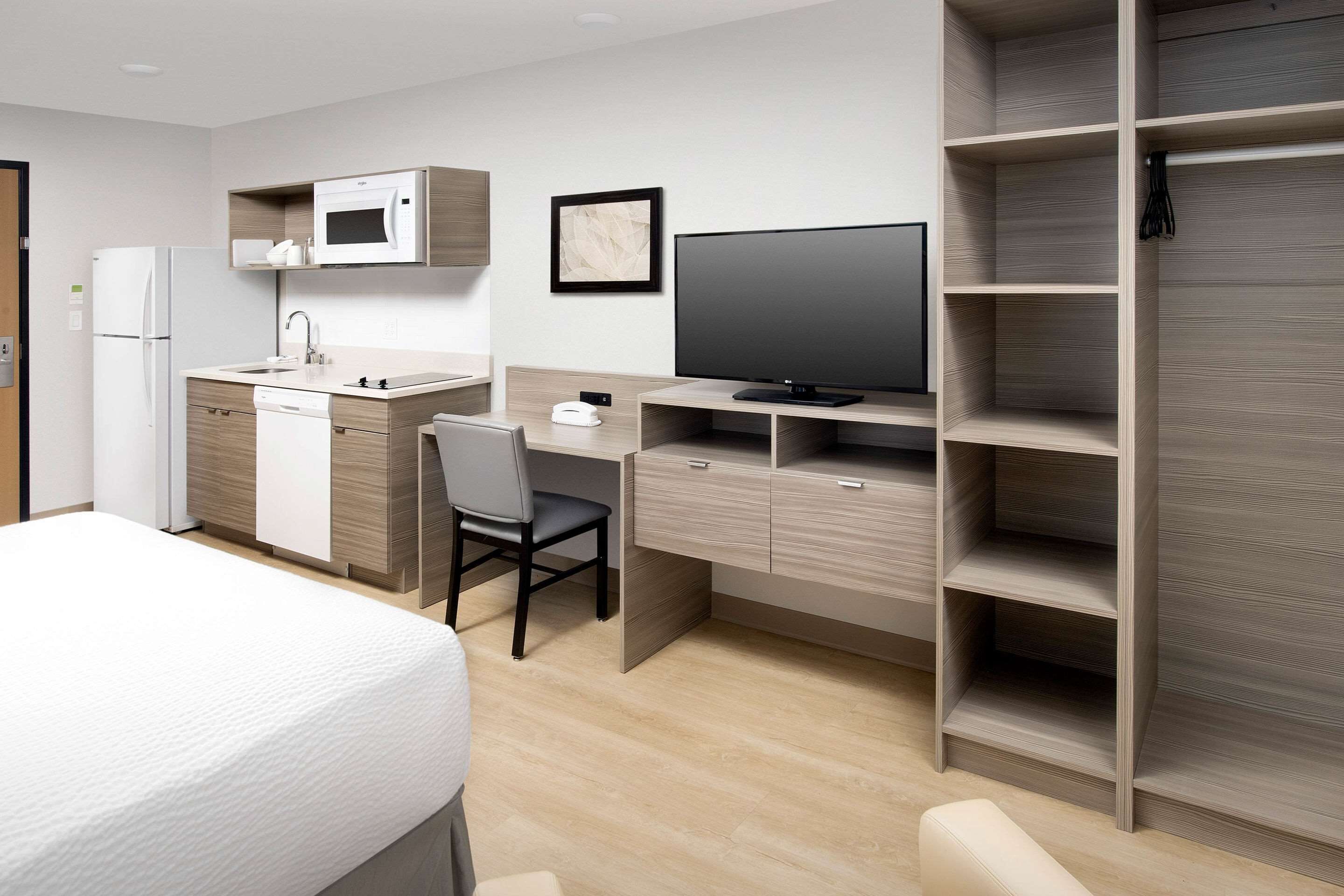 A modern hotel room with a kitchenette, a flat-screen TV, a desk, and a wardrobe.