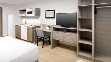 A modern hotel room with a kitchenette, a flat-screen TV, a desk, and a wardrobe.