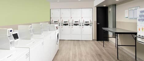 A laundry facility with multiple washing machines and dryers, a table, and a door leading to another room.