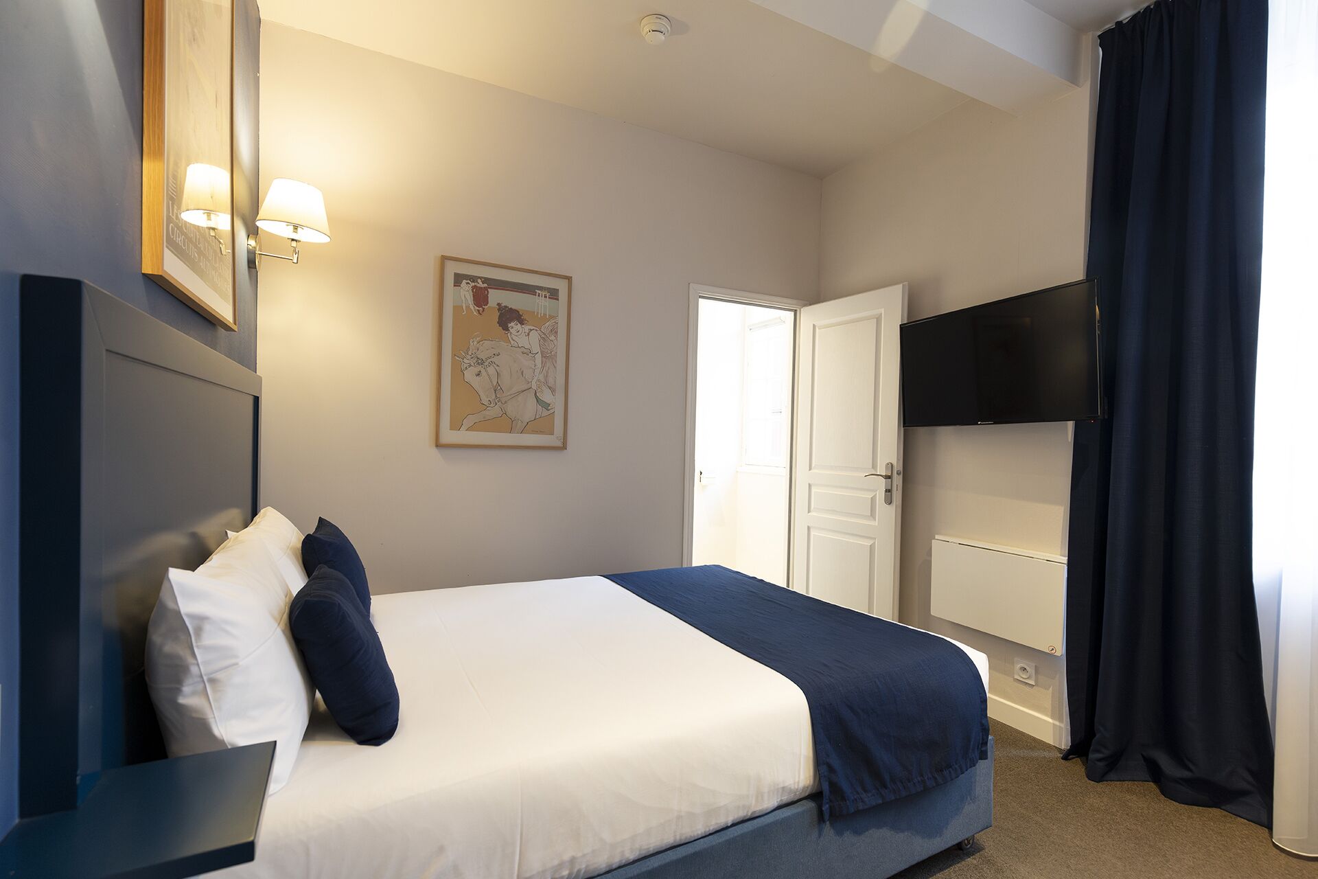 A hotel room with a bed, a flat-screen TV, a painting, and a door.