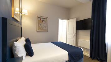 A hotel room with a bed, a flat-screen TV, a painting, and a door.