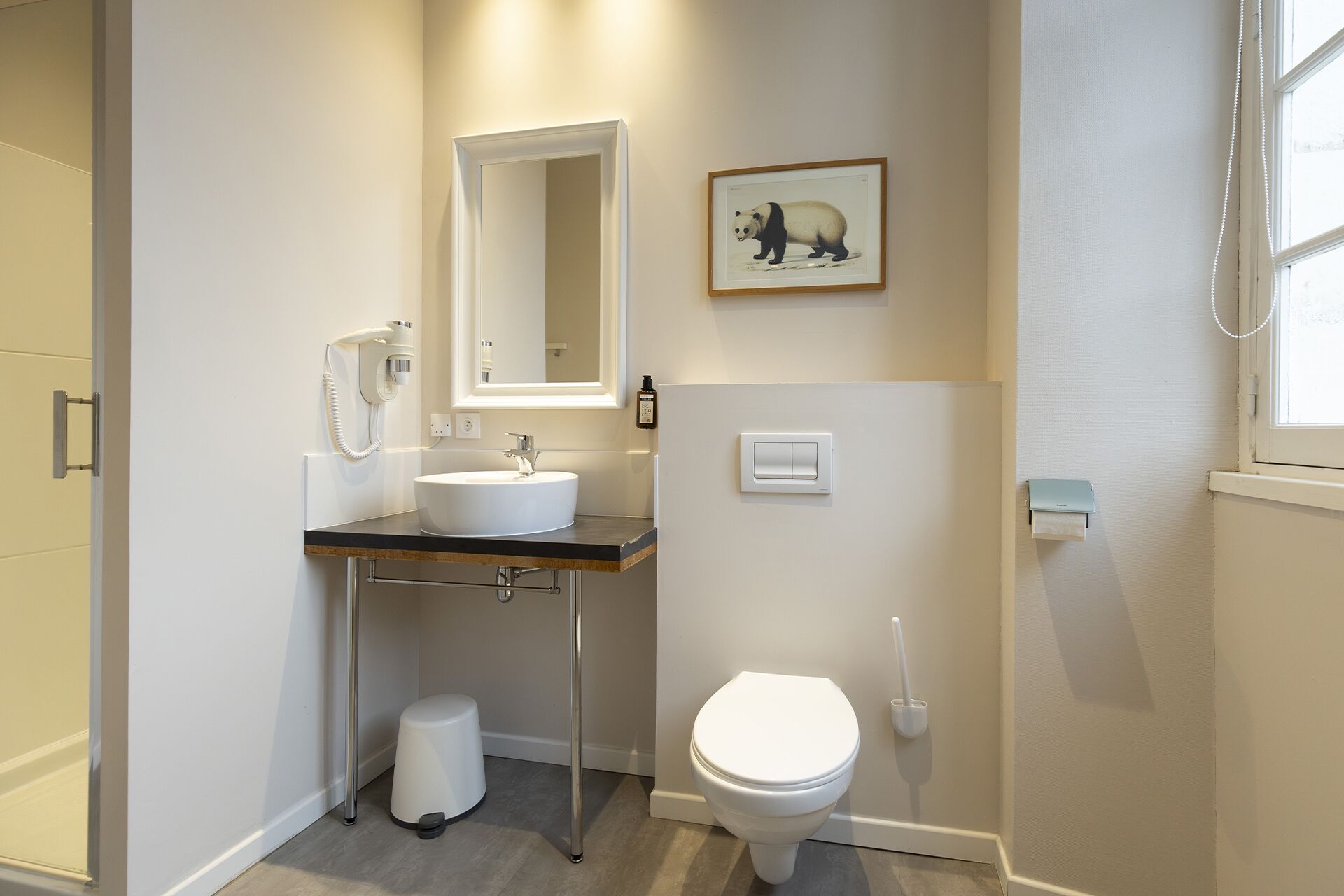 A modern bathroom with a white sink, mirror, and toilet. There is a framed picture of a panda on the wall.