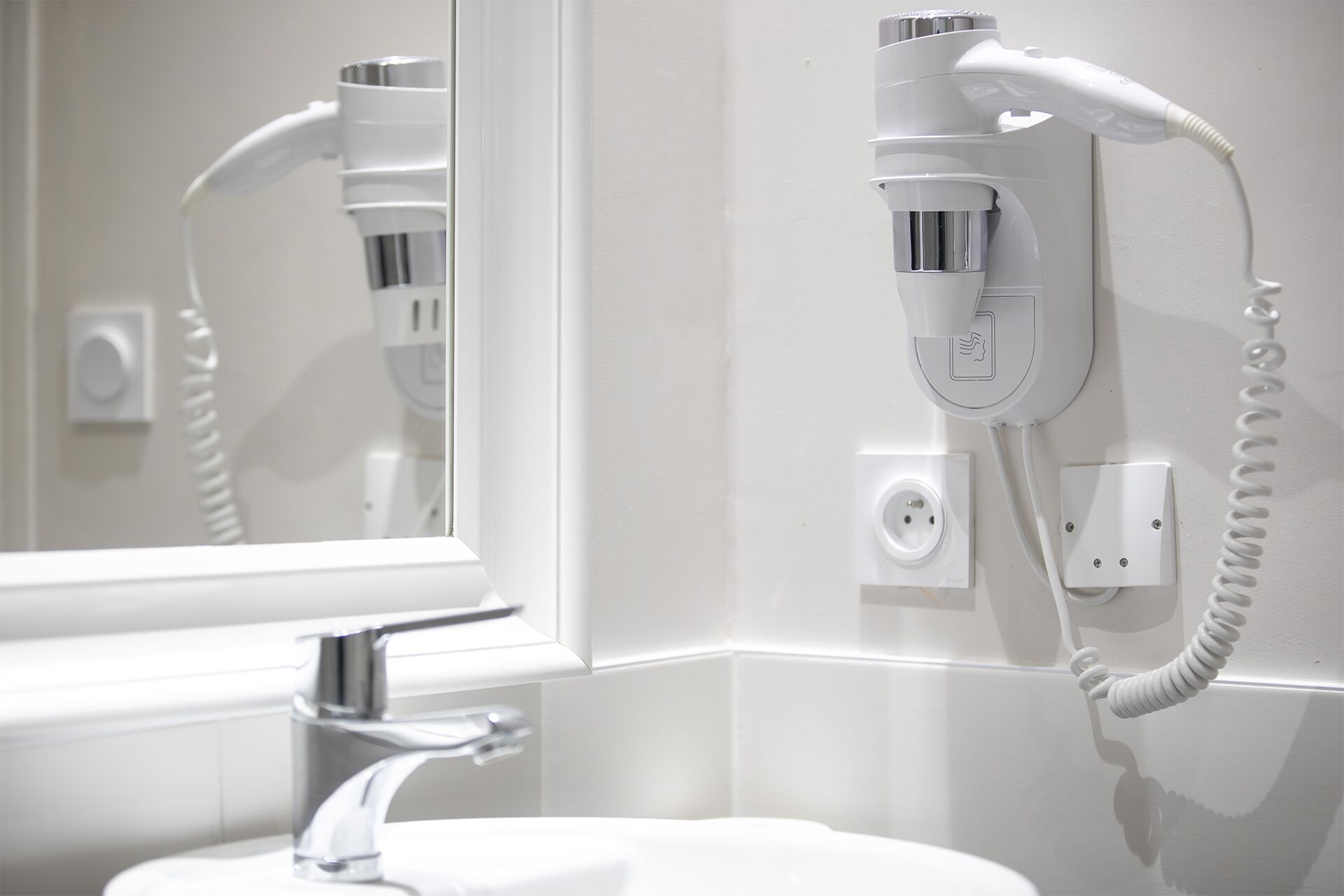 A bathroom with a hairdryer mounted on the wall, a mirror, and a sink.