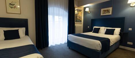 Habitación de hotel con dos camas, un ventanal con cortinas translúcidas e iluminación en la pared.