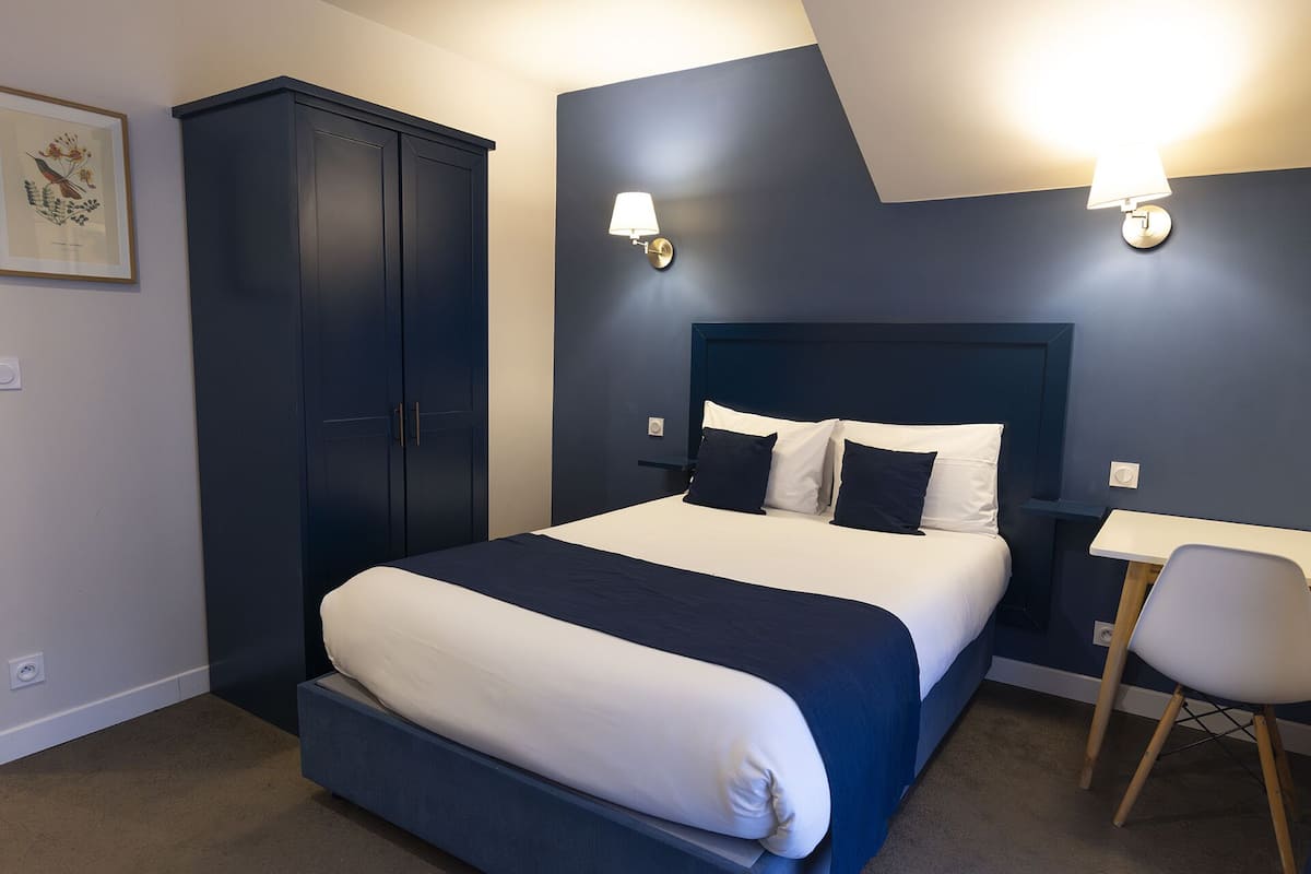 Un dormitorio con una cama, un armario, un escritorio y dos lámparas fijadas a la pared.