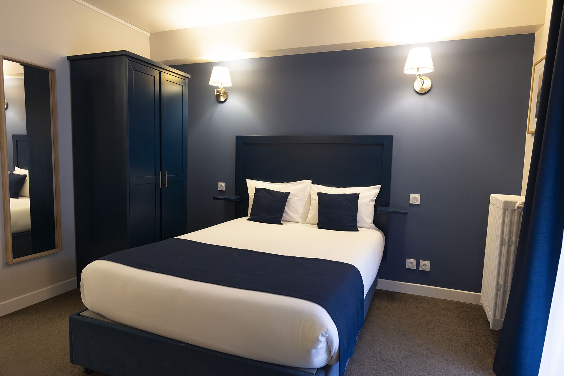 Quarto bem arrumado com uma cama grande, paredes escuras e duas luminárias fixadas na parede.