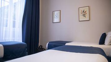 Habitació d'hotel amb dos llits, un finestral gran amb cortines primes i dos quadres amb motius botànics a la paret.