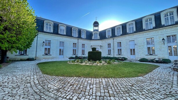 Een binnentuin met een geplaveid pad, een centrale tuin en een groot gebouw met meerdere ramen en een toren.