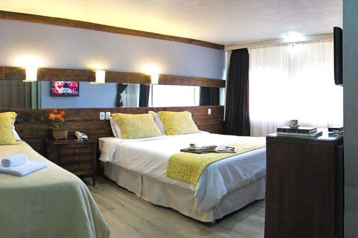 Habitación de hotel con dos camas, televisión, escritorio y ventana con cortinas.