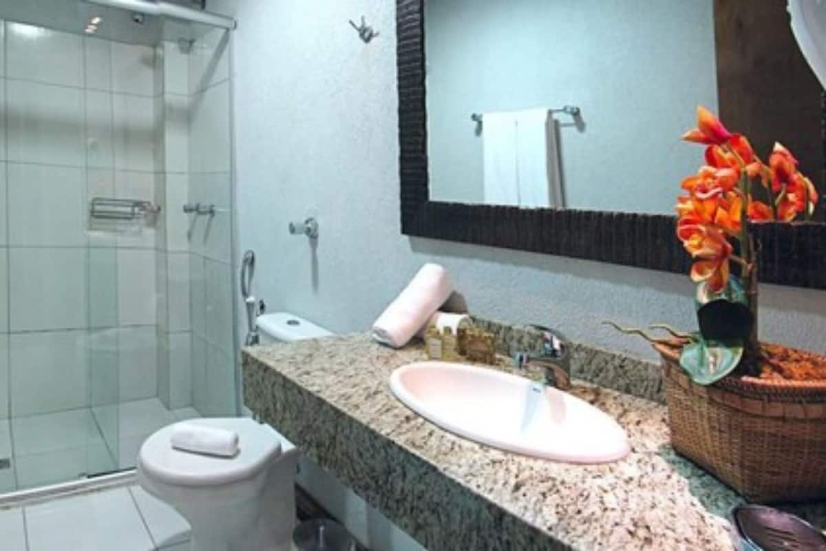 Un baño con cabina de ducha de vidrio, inodoro blanco, lavamanos con lavabo rosa y espejo con una toalla colgada en la pared.