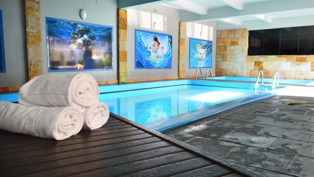 A swimming pool with a stone-tiled deck, towels, and artwork on the walls. - Sky Centro Hotel & Spa (Gramado)