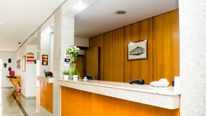 A hotel reception area with a marble counter, wooden paneling, a framed picture, and a potted plant.