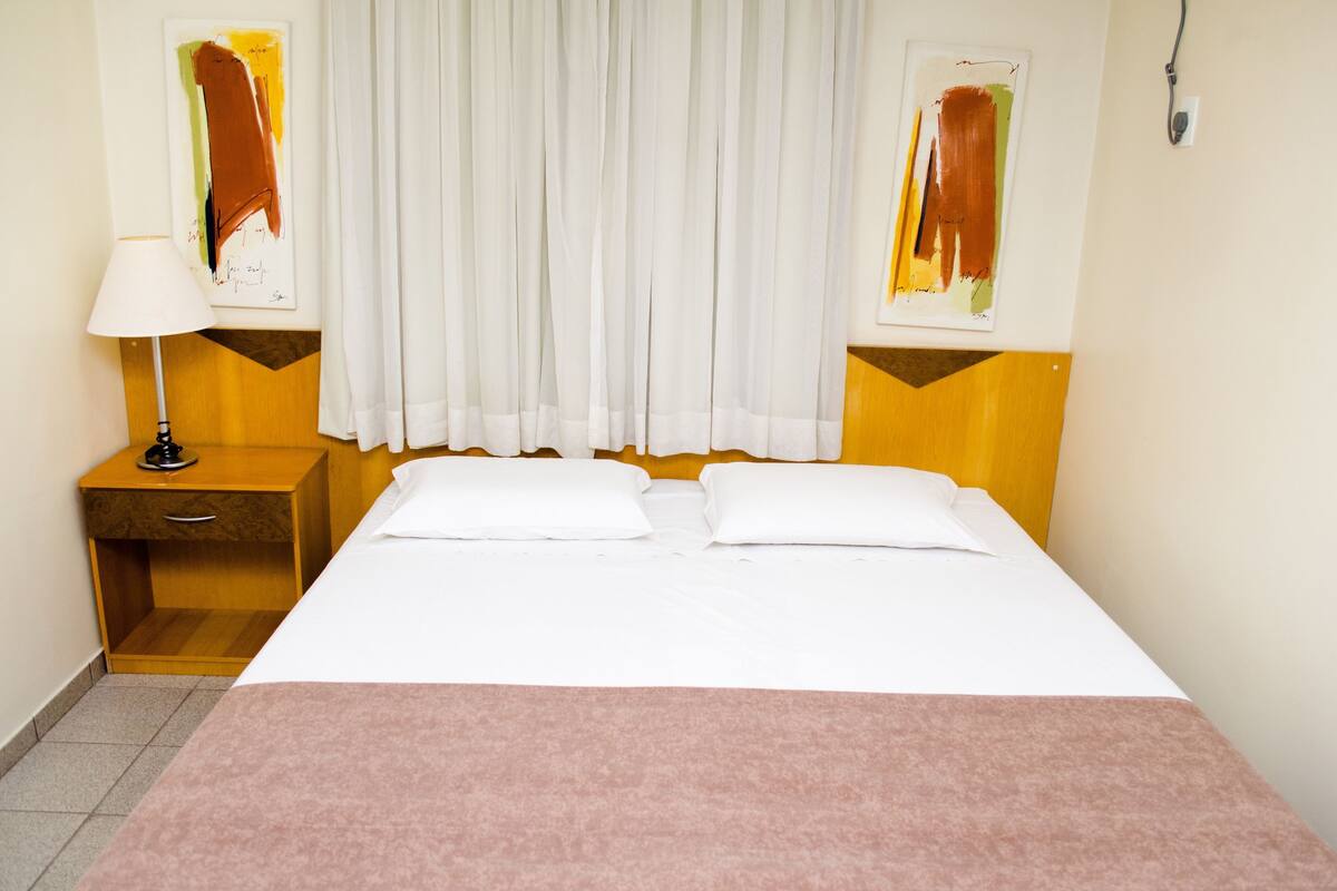 Een hotelkamer met een bed, een nachtkastje, een lamp en twee abstracte schilderijen aan de muren.