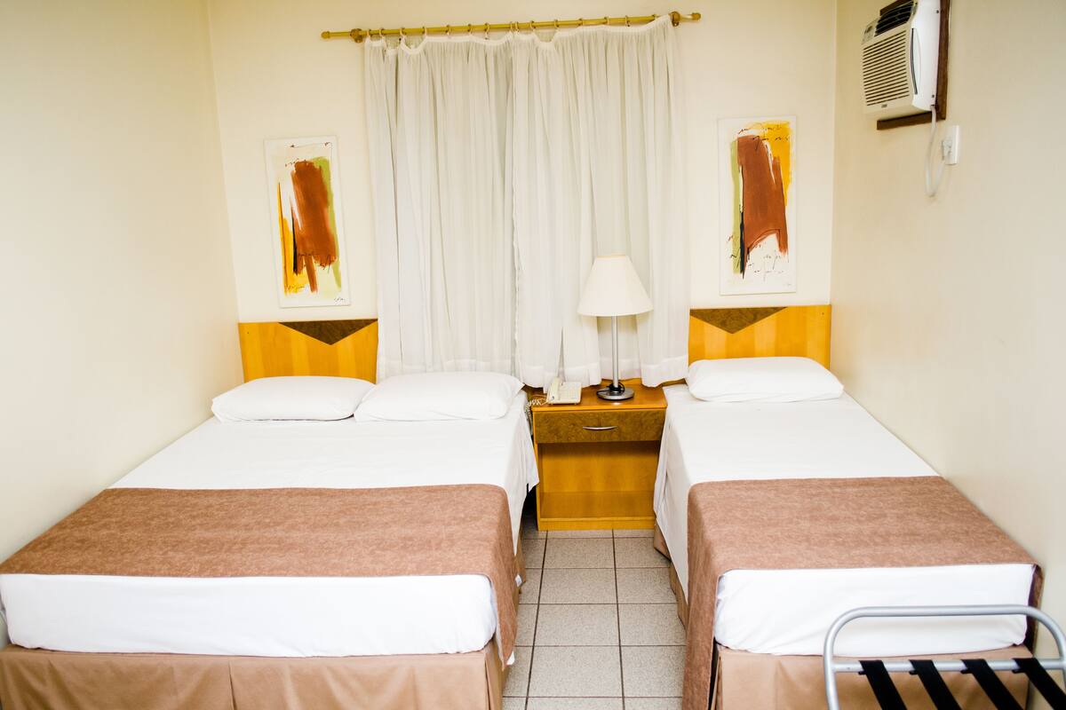 Een hotelkamer met twee bedden, een nachtkastje met een lamp en een raam met gordijnen.