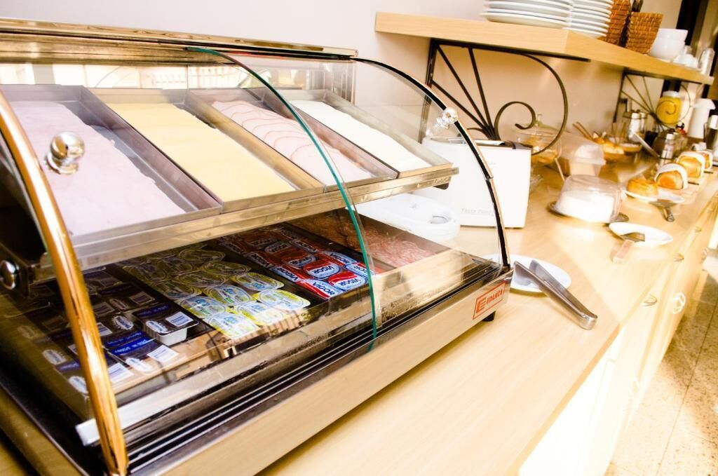 Um refrigerador com diversos alimentos embalados, um registradora e um balcão com pratos e utensílios.