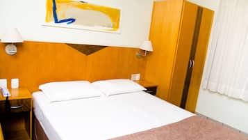 A hotel room with a bed, a nightstand, a lamp, a wardrobe, and a painting on the wall.