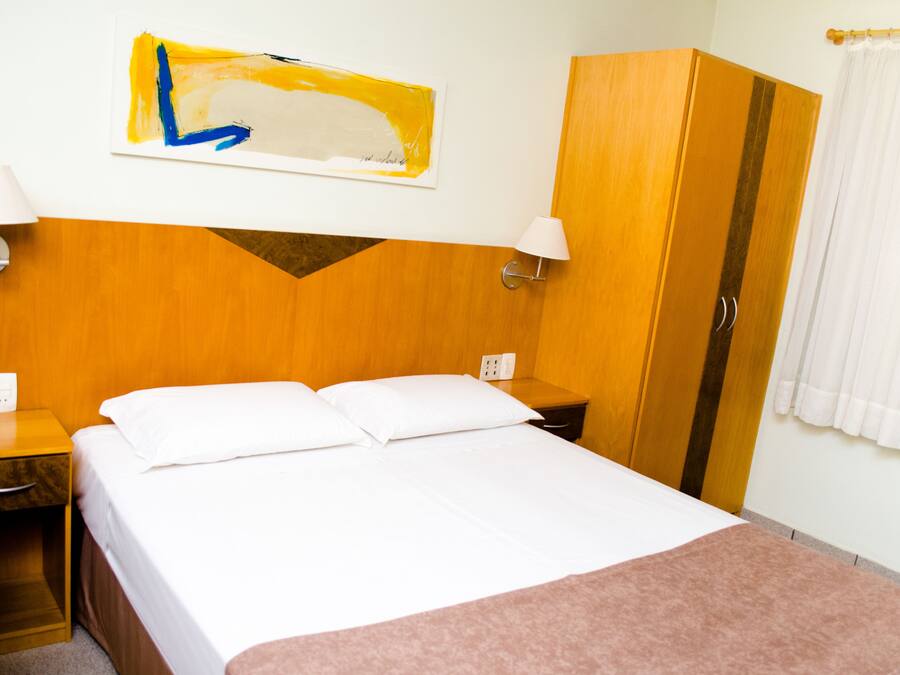 A hotel room with a bed, a nightstand, a lamp, a wardrobe, and a painting on the wall.