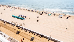 Een strand met een houten promenade, parasols en mensen.