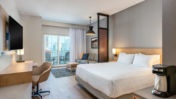 Une chambre d’hôtel moderne équipée d’un grand lit, d’un bureau, d’une chaise, d’une machine à café et d’une télévision.