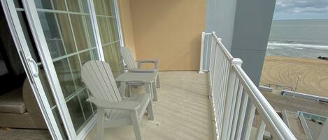 A balcony with two Adirondack chairs, a small table, and a view of the beach.